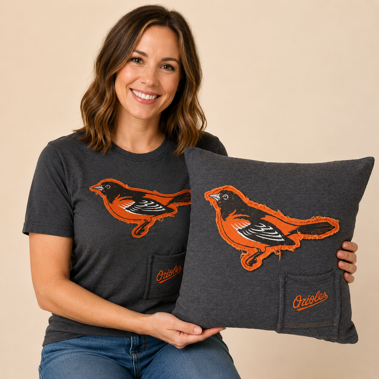 Smiling woman wearing a dark gray Orioles T-shirt and holding the matching memory pillow with a decorator pocket.