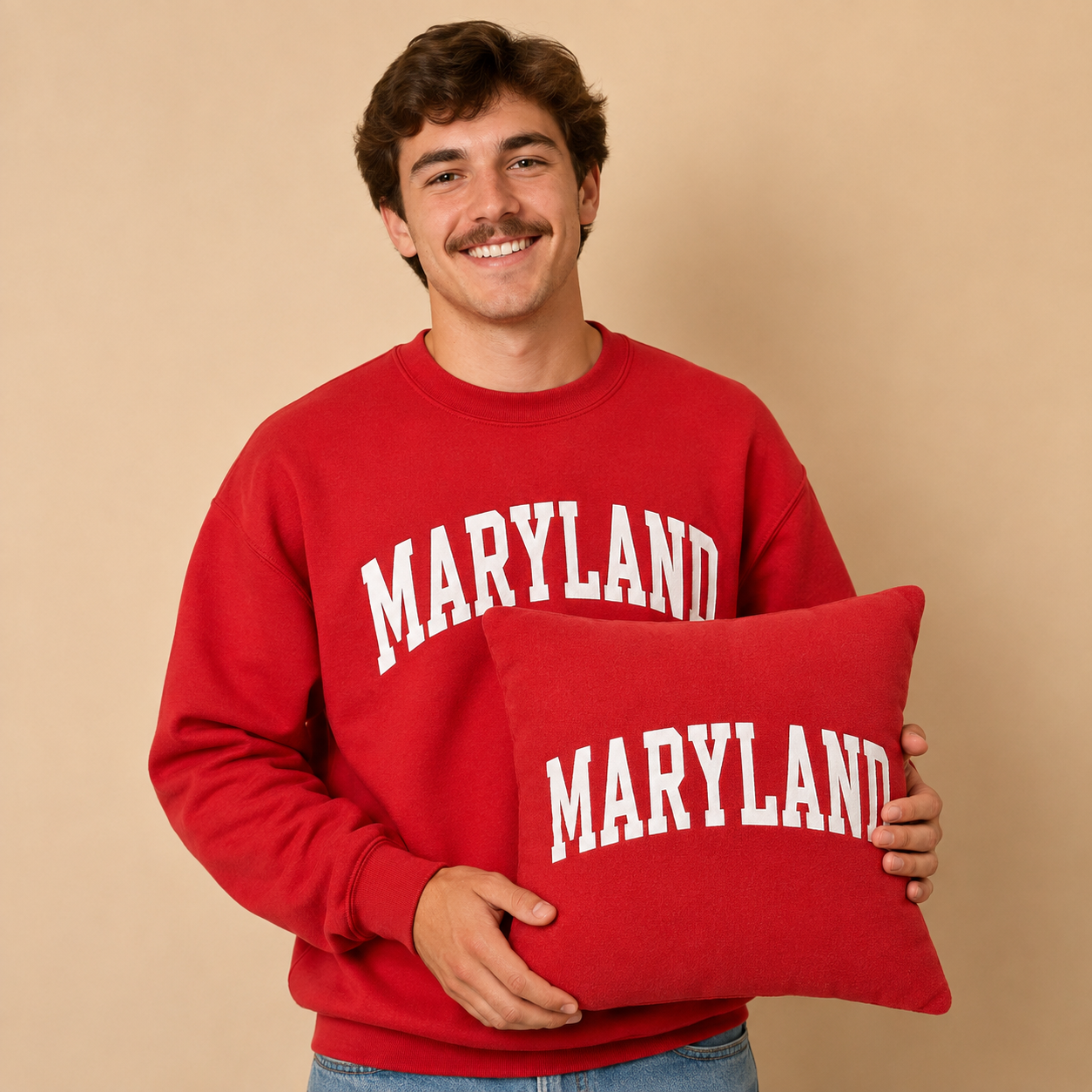 Young man with brown hair and a mustache wearing a red Maryland sweatshirt and holding the matching memory pillow.